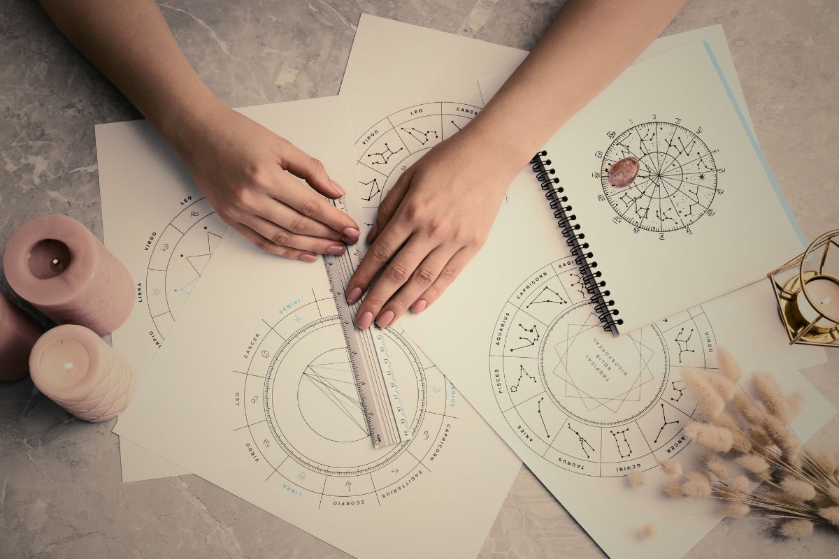 A hand tracing various astrology charts, surrounded by candles & flowers