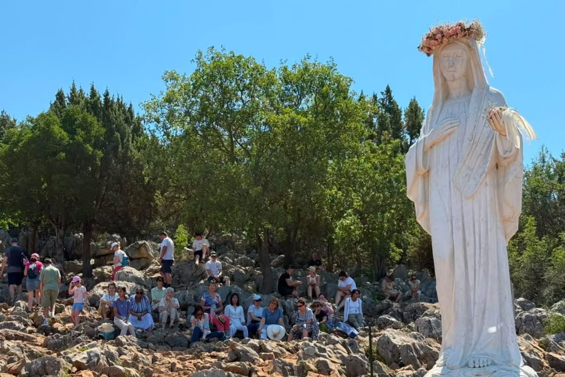 Pilgrims gathered in quiet reflection beside the statue of Our Lady on Apparition Hill in Medjugorje, Bosnia and Herzegovina.